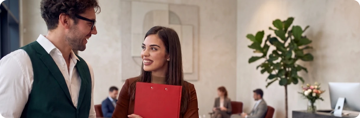 Two colleagues talking in an office lobby, one holding a folder