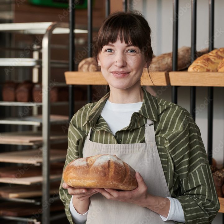 A baker holding a fresh loaf in her shop